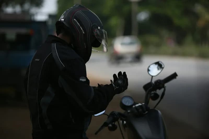 Motard en casque et veste de protection enfilant ses gants à côté de sa moto