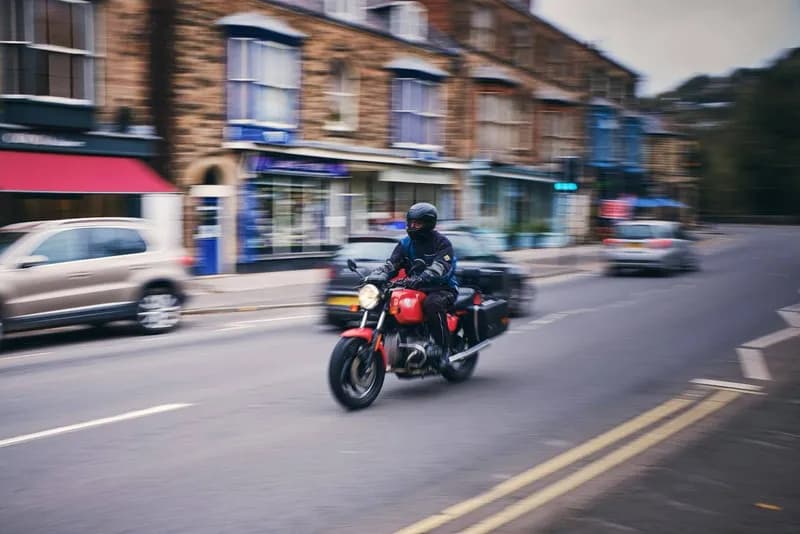 Motard en tenue complète sur une moto ancienne dans une rue commerçante
